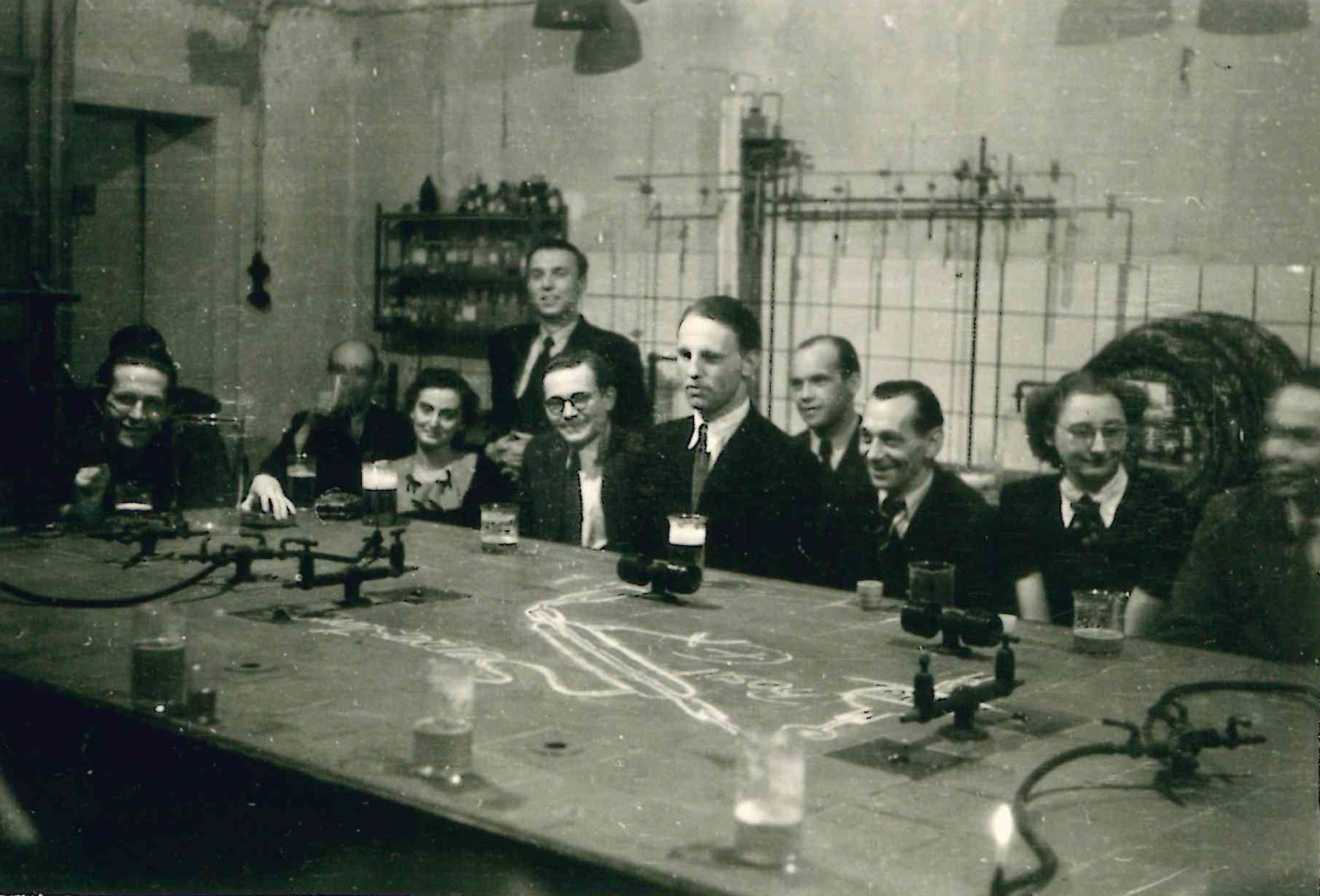 Einige Personen sitzen im Labor mit Bechergläsern um einen Tisch